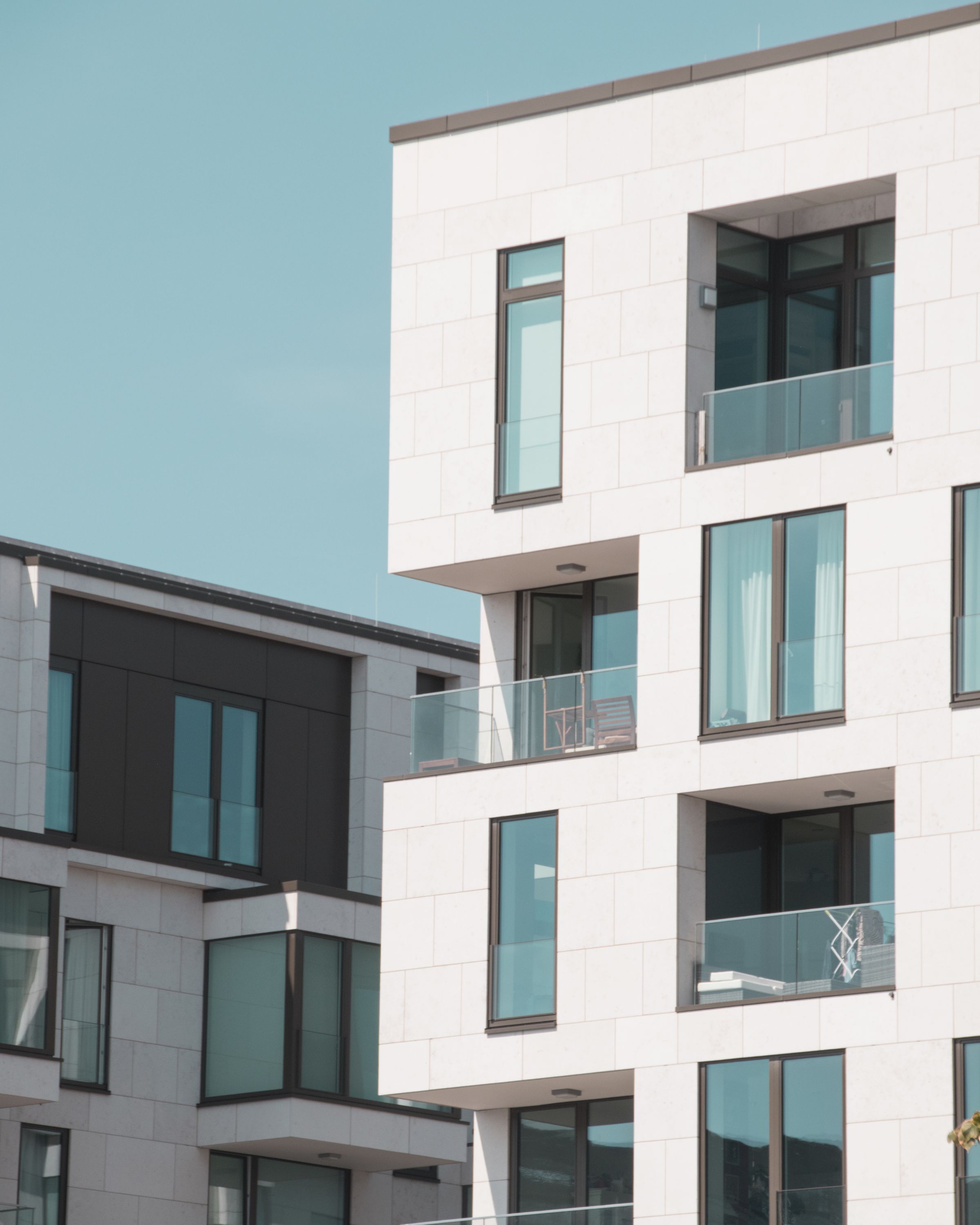 Weiße Neubaufassade mit Glasbalkonen vor blauem Himmel
