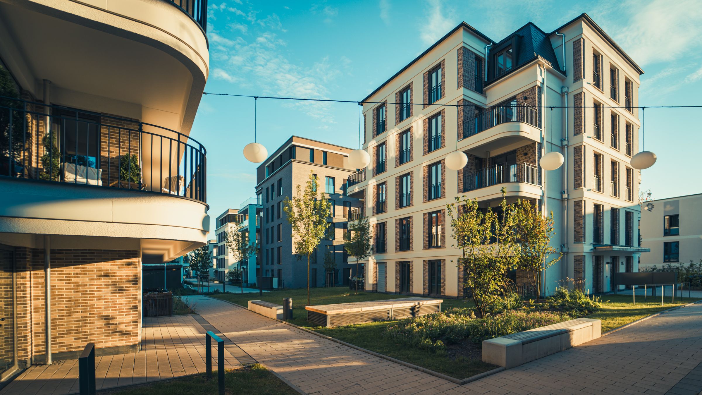 Neubauquartier mit hellen Wohnhäusern, Balkonen und begrüntem Innenhof im Abendlicht